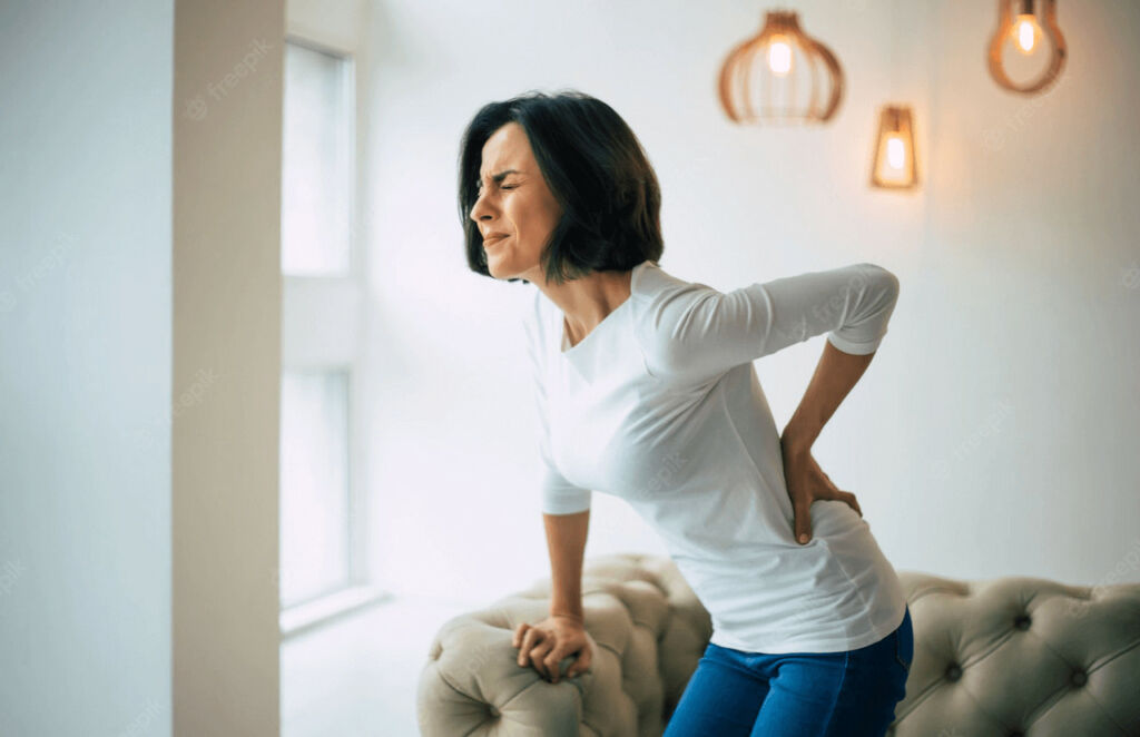 Woman holding lower back in pain - Misaligned Spinal Vertebrae